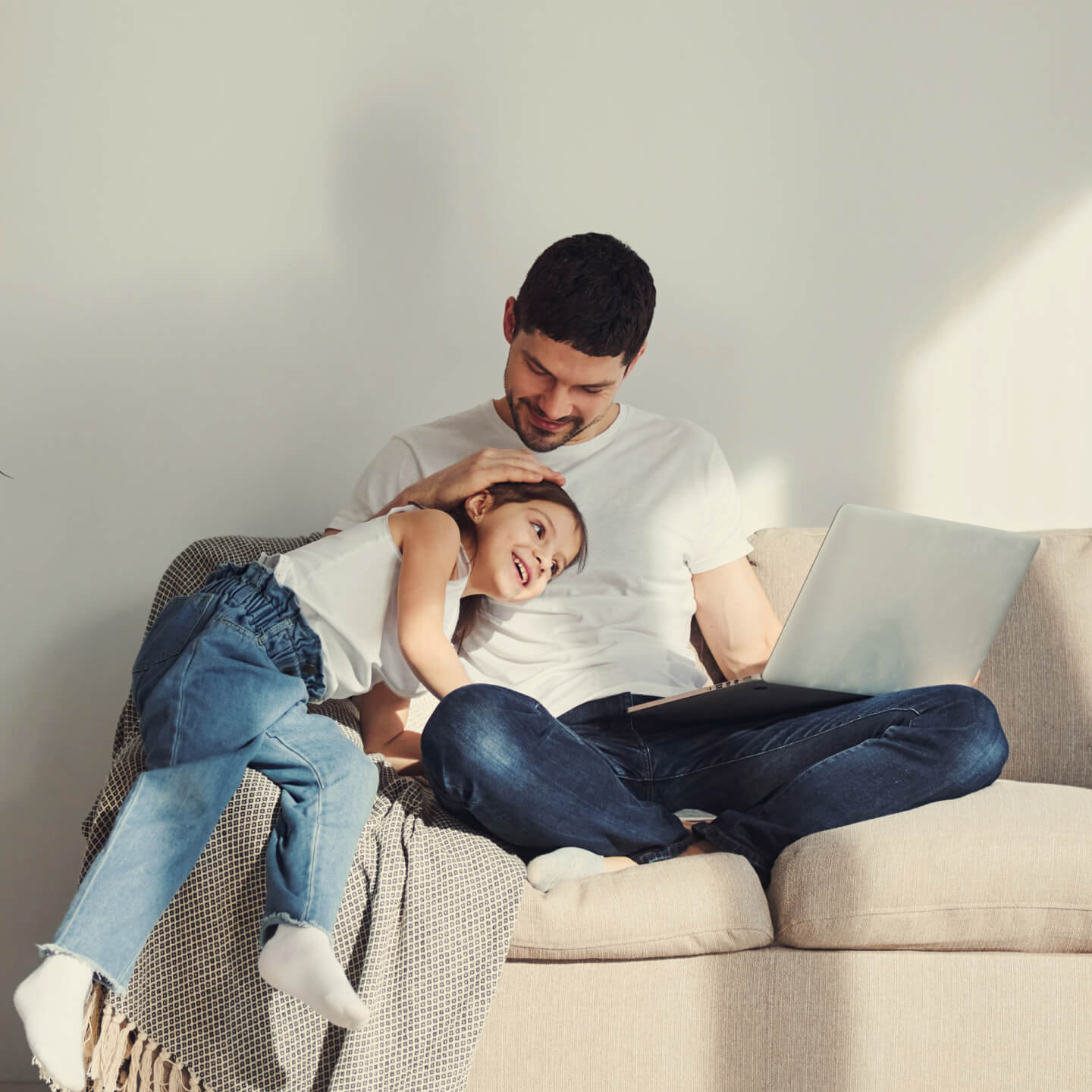Un père est assis sur un sofa, sa fille assise sur l’accoudoir, la tête sur sa poitrine, et il la serre affectueusement.