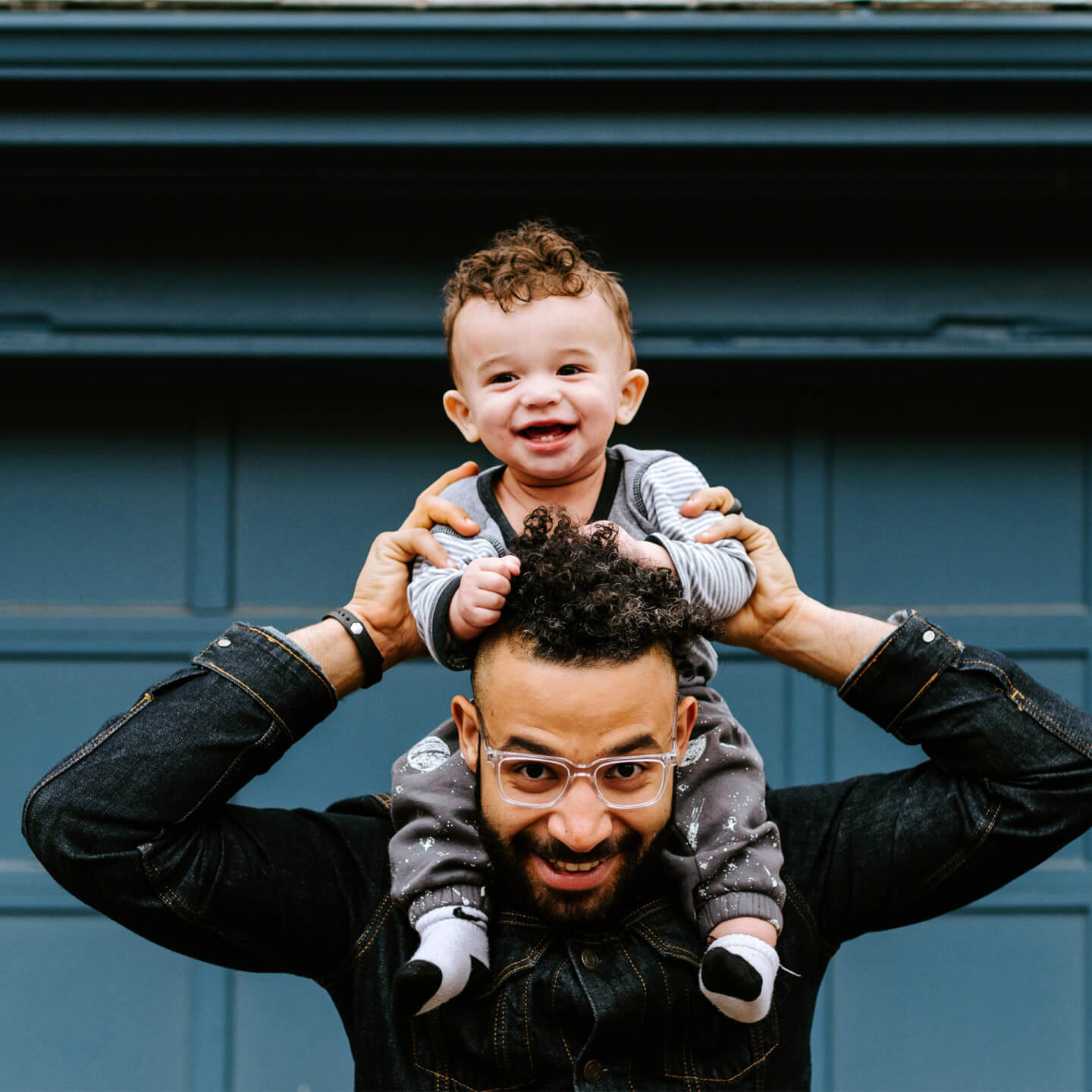 A child sitting on his father’s shoulders, both smiling and enjoying a fun moment together.