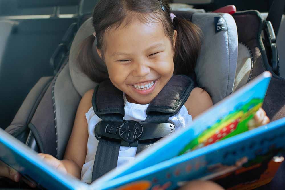 Une jeune fille lit un livre dans son siège d'auto