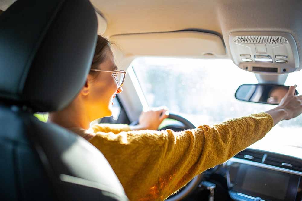 Rear view portrait of young woman driver adjusting rear view mirror of car while driving in the city