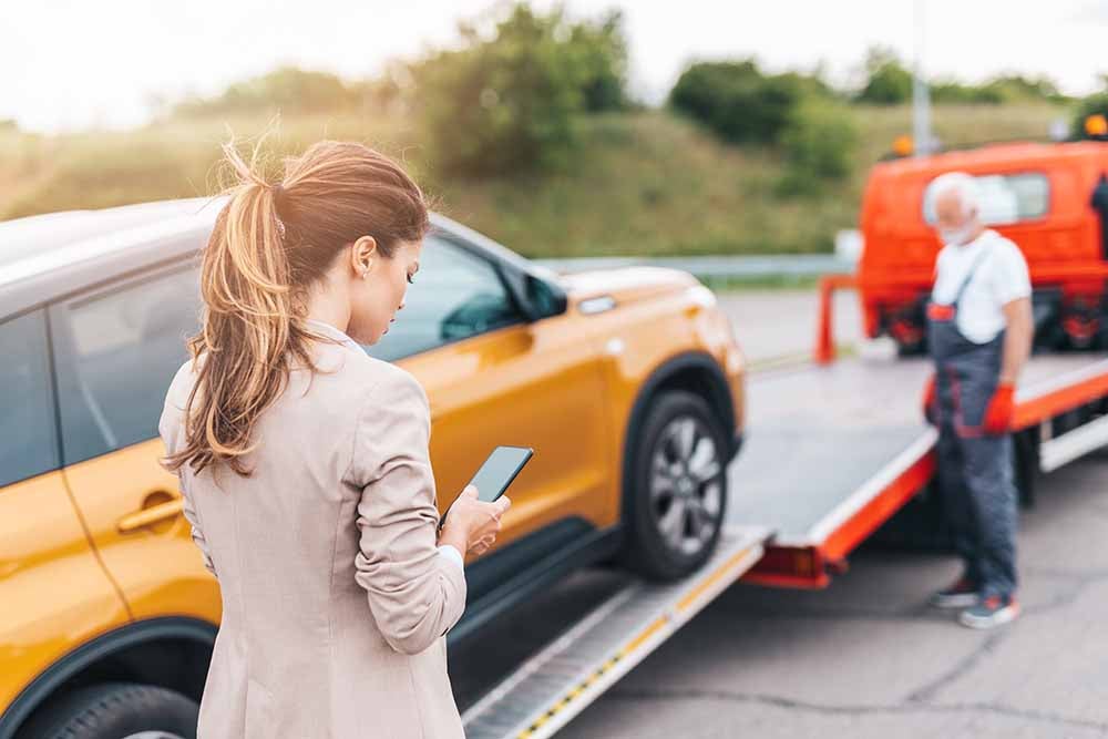 Woman contacting her insurer while her car gets towed