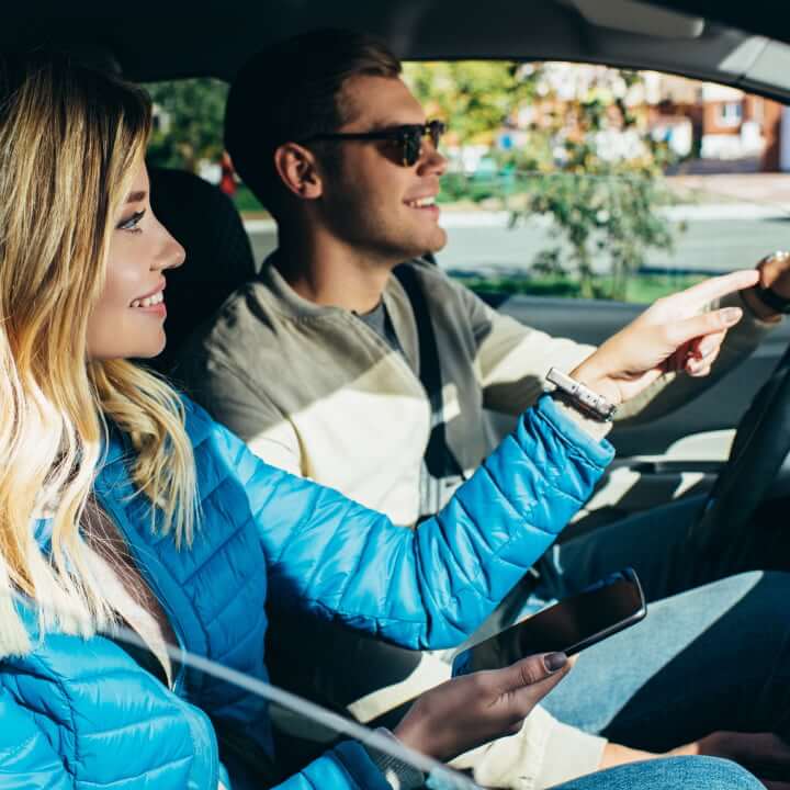 Smiling woman with a smartphone helping her boyfriend who is driving a car navigate the streets of Ottawa.