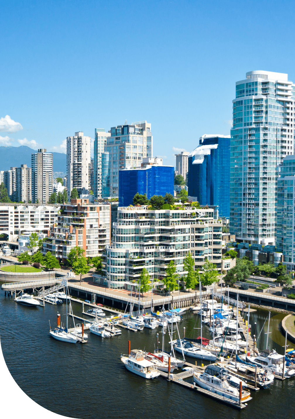 Un paysage urbain montrant des condos en Colombie-Britannique qui surplombent l’océan avec les montagnes en arrière-plan.