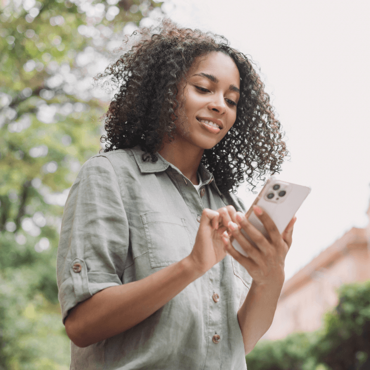 Une jeune femme se procure de l’assurance en ligne sur son téléphone tout en faisant une randonnée au parc.